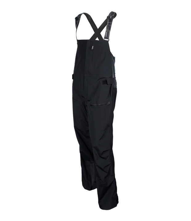 A pair of black shell bib pants with intergrated suspenders, full-length side zip, a zippered chest pocket, thigh pockets with cover flap and a side adjuster.