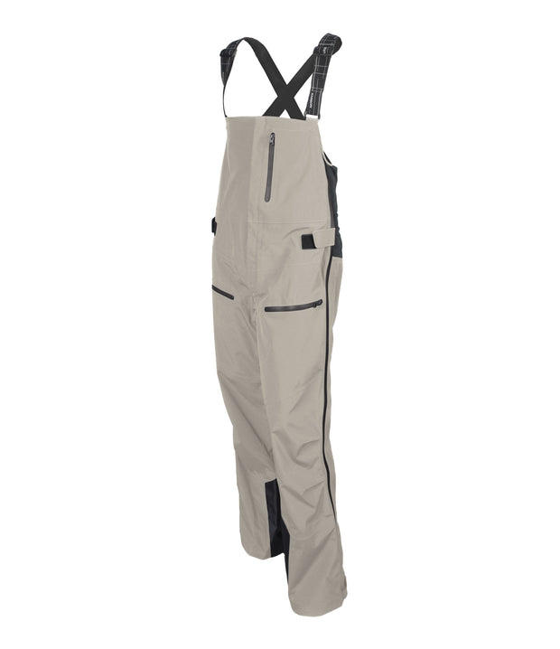 A pair of beige shell bib pants with intergrated suspenders, full-length side zip, a zippered chest pocket, thigh pockets with cover flap and a side adjuster.