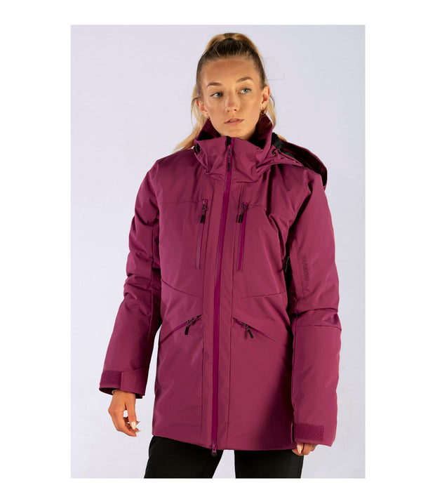 A woman waring a purple insulated jacket featuring a front zip closure, two zippered chest pockets, a sleeve pocket and two side zip pockets with an adjustable hood.