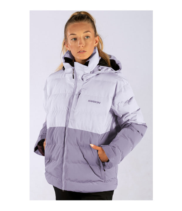 A woman wearing a two-toned insulated puffer with light purple upper body and darker purple lower body, featuring a front zip closure, zippered chest pocket, and two side zip pockets, with an a hood.