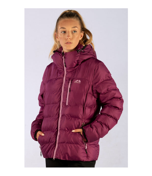 A woman wearing a women's pink puffer featuring a front zip closure, zippered chest pocket, and two side zip pockets, with an adjustable hood.