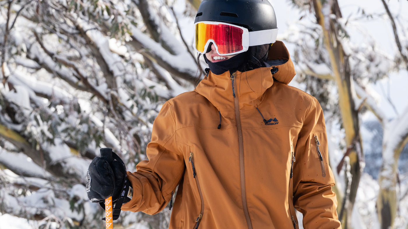 A women wearing a brown jacket and helmet with goggles in a snowy landscape